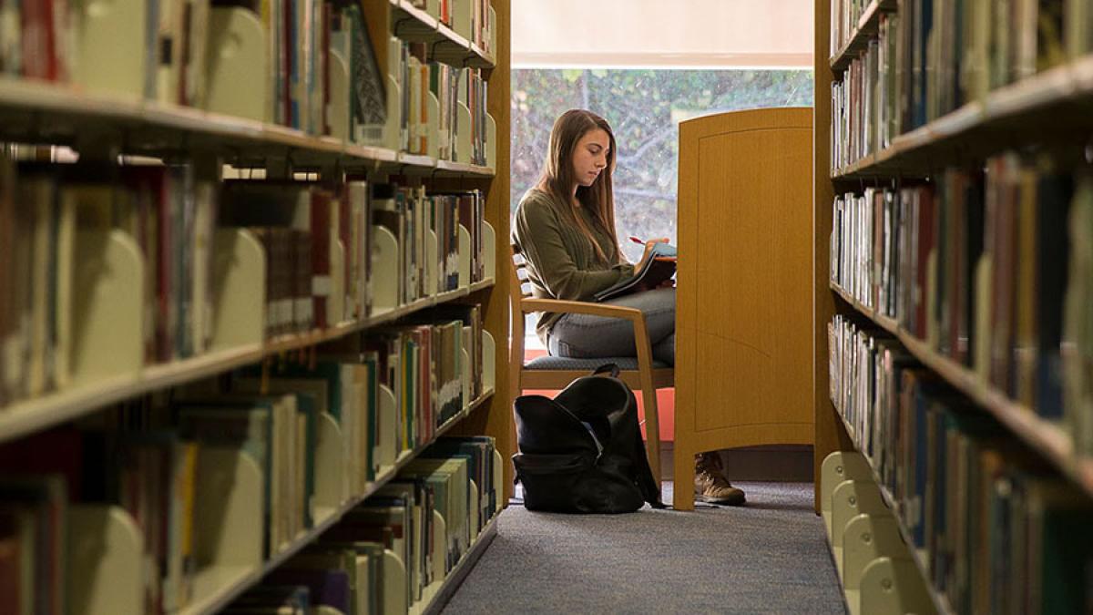 Student sitting at a study desk down the stacks of a library