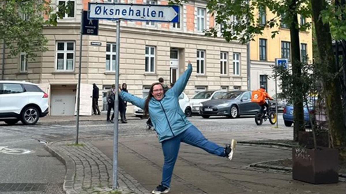 Pace University Lubin student in front of a street sign in a leafy neighborhood of Copenhagen during a 2023 field study to Denmark and Sweden