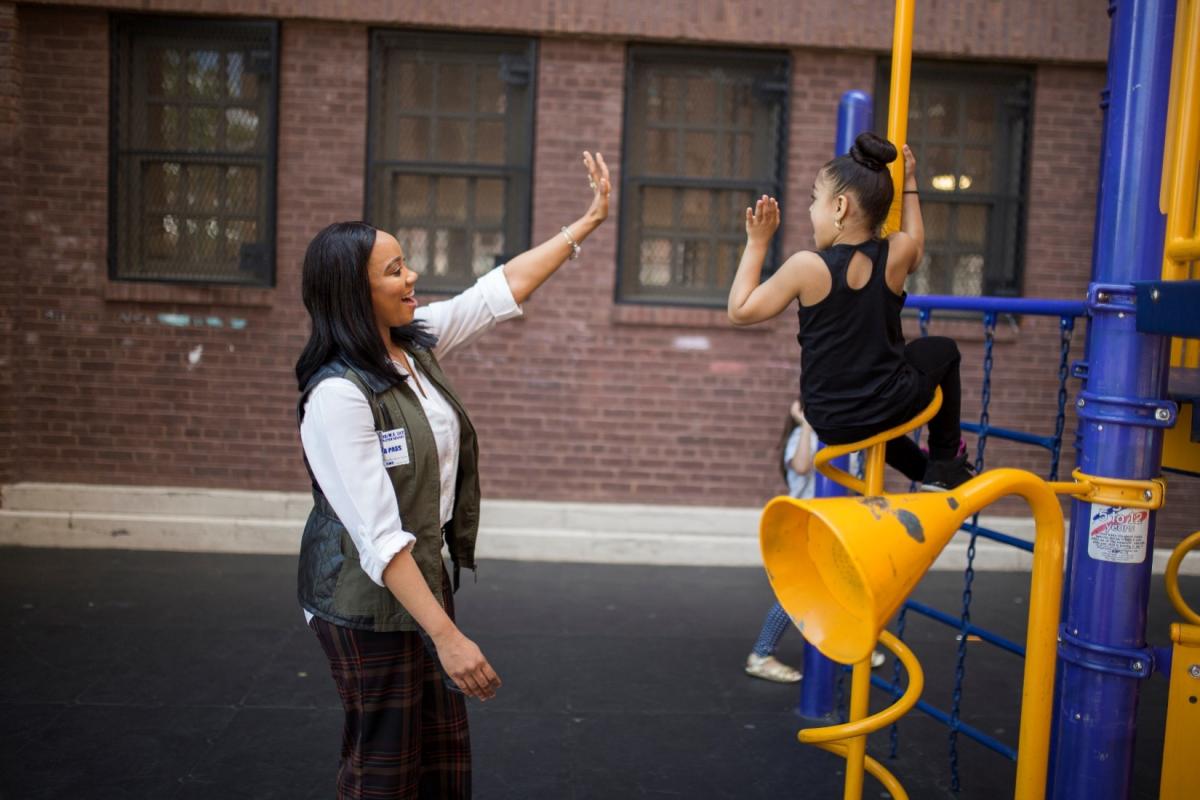 Student teacher high-fiving a girl on the playground.