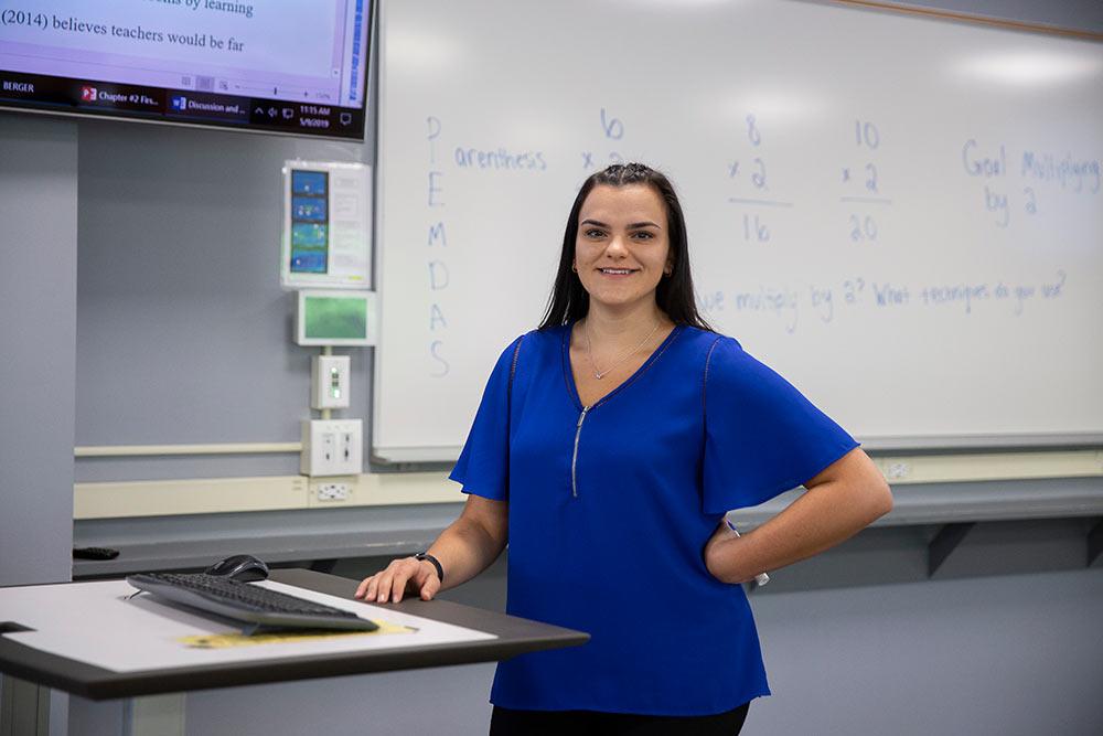 School of Education student standing in a classroom smiling at the camera.