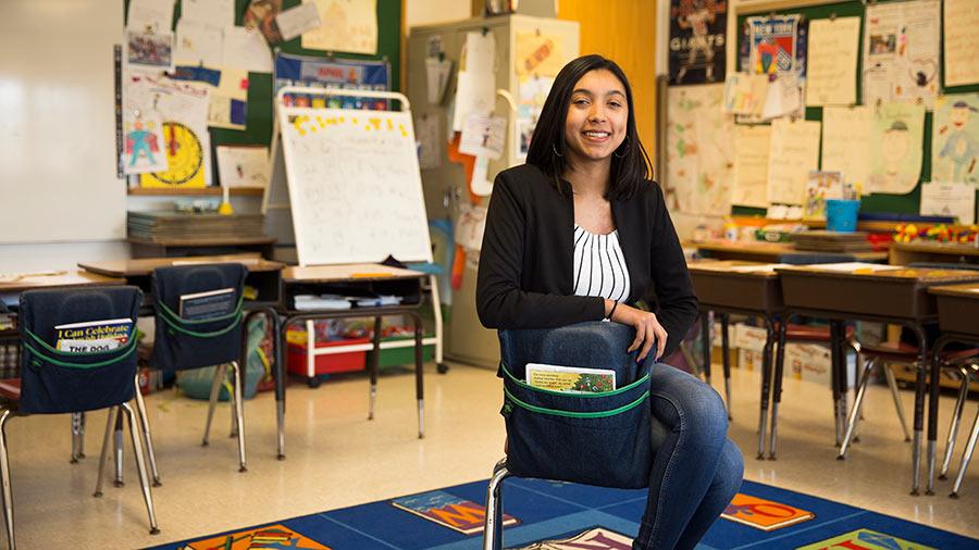 Student sitting on a chair in a classroom smiling at the camera.