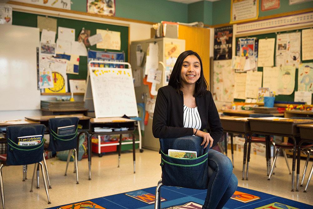 Student teacher sitting in a classroom smiling at the camera.