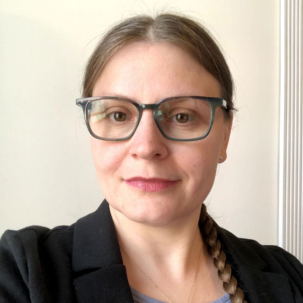 A headshot of faculty member April Bartlett, with blonde hair pulled back and black-framed glasses