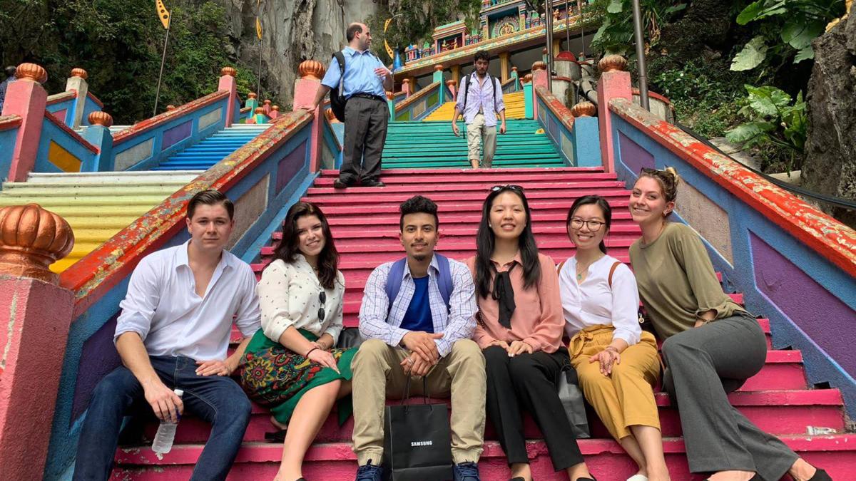Six Pace University Lubin students sitting on the steps of a temple in Malaysia during a 2019 field study to Singapore and Malaysia