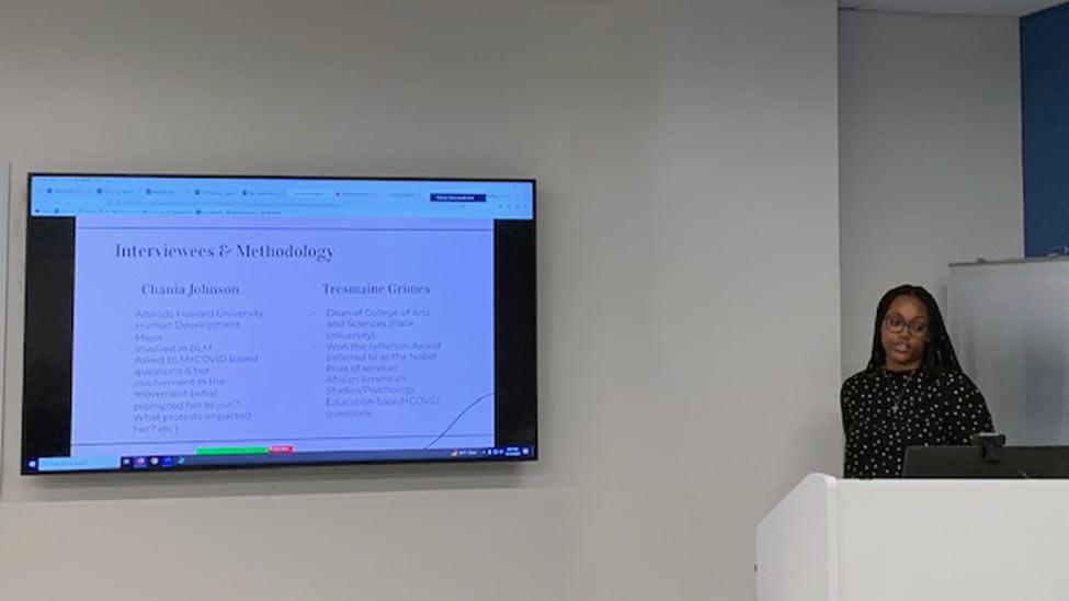 young woman at a podium presenting a powerpoint presentation