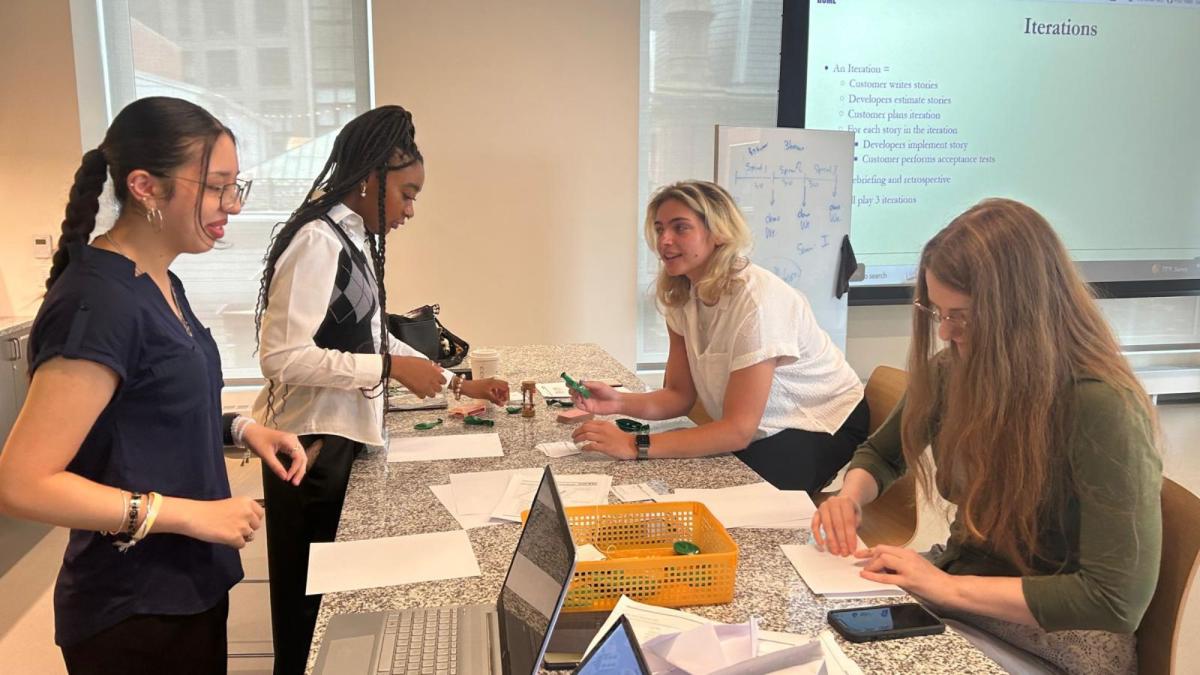 Pace Seidenberg students sitting around a table at the NYC Design Factory space, talking about the project they are developing.