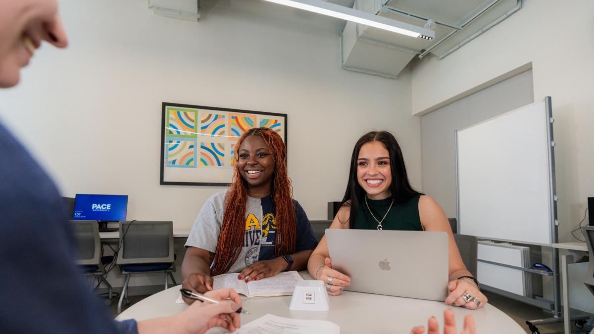 Two Pace students sitting at table conversing with instructor