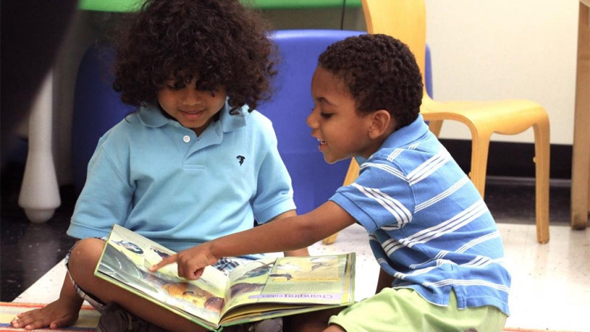 Two little boys reading a book.