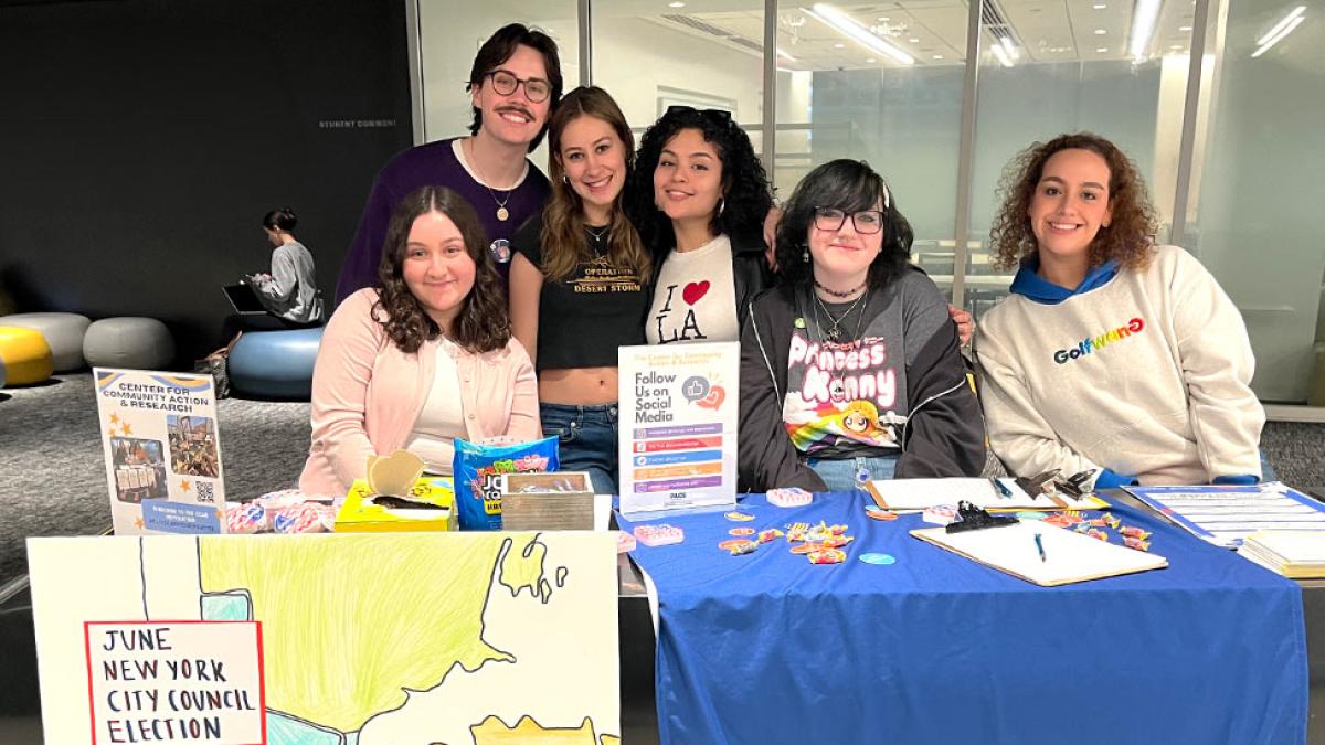 Several students at a table with Center for Community Action and Research materials and a poster of the June City Council Election