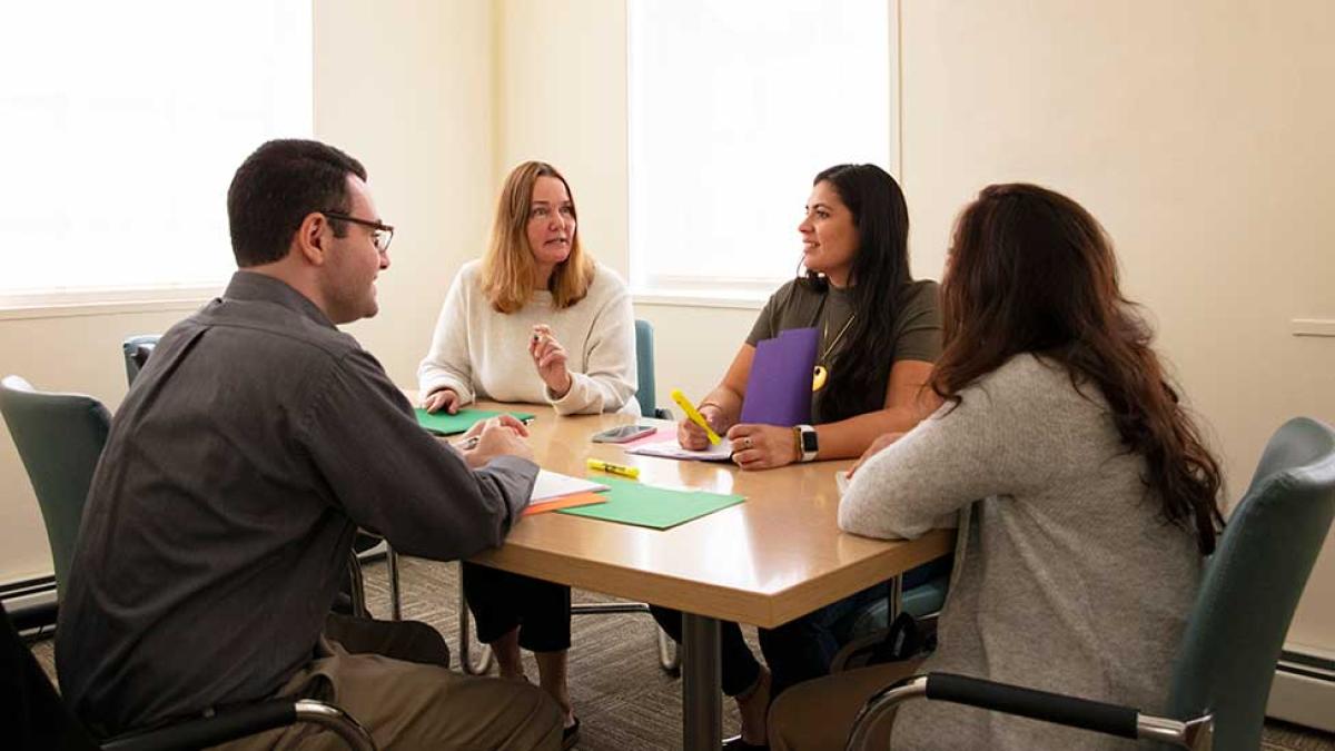 four students talking at a meeting around a table