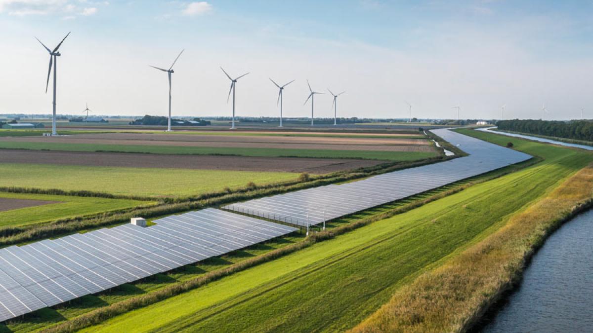 Row of wind turbines next to a river and a farm