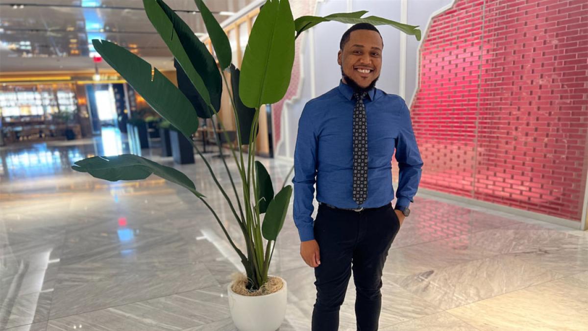 Lubin alumnus Steven Anglade '23 standing in the lobby of his office building at the nonprofit Rising Groundat 