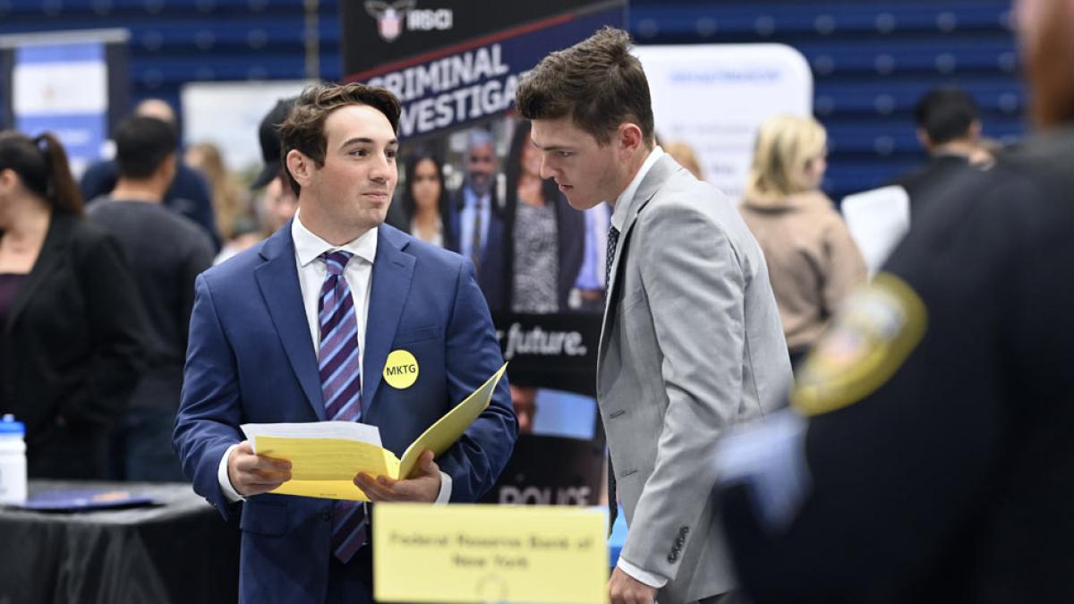 Two Pace students in suits looking over their resumes at the Career Fair. 