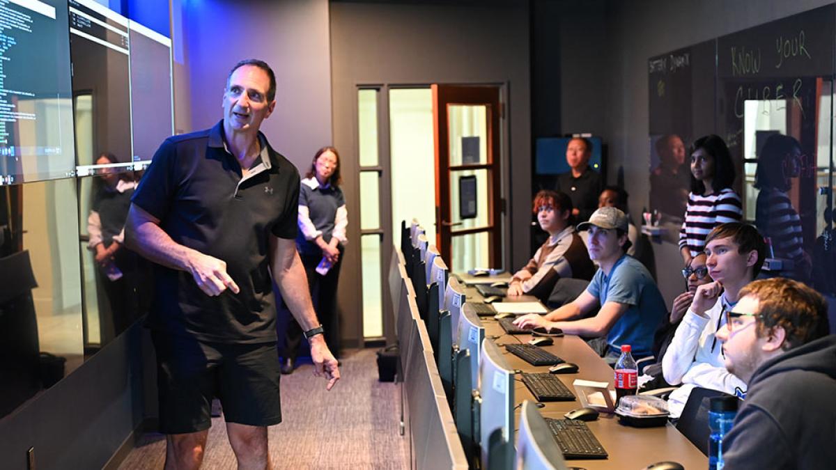 Pace pofessor standing in front of a wall of screens as students watch him. 