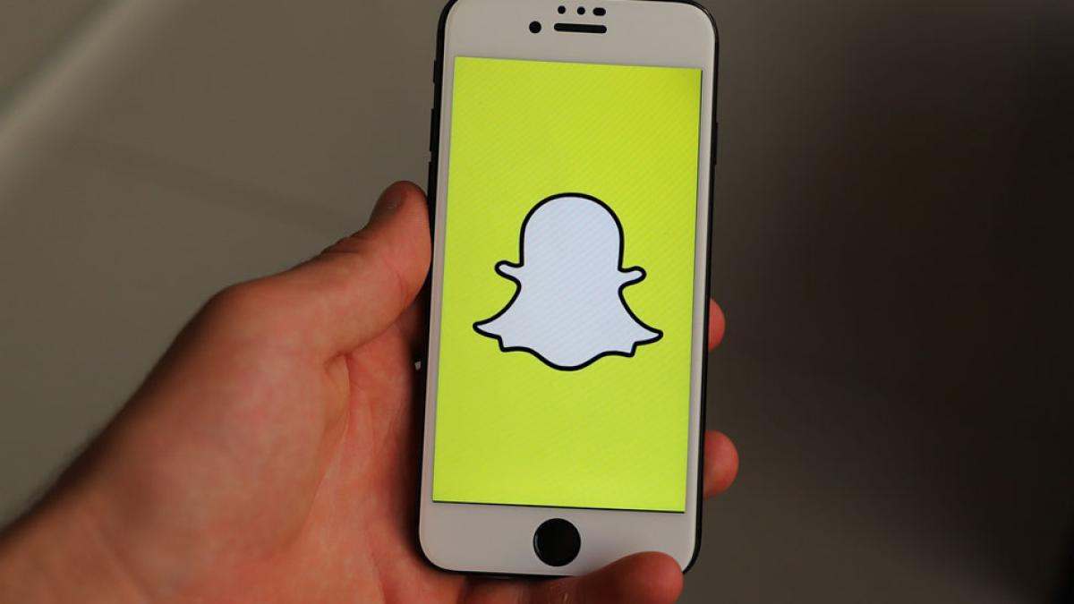 closeup of hand holding mobile phone screen displaying the Snapchat logo