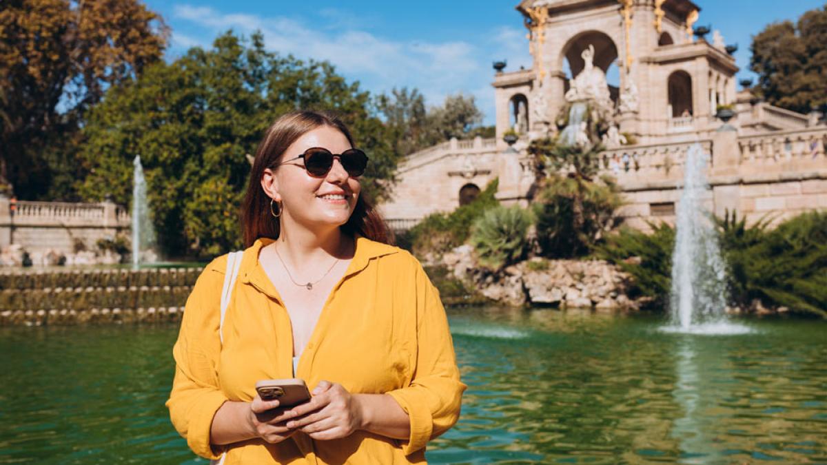 young woman in sunglasses posing in front of a Spanish fountain. 
