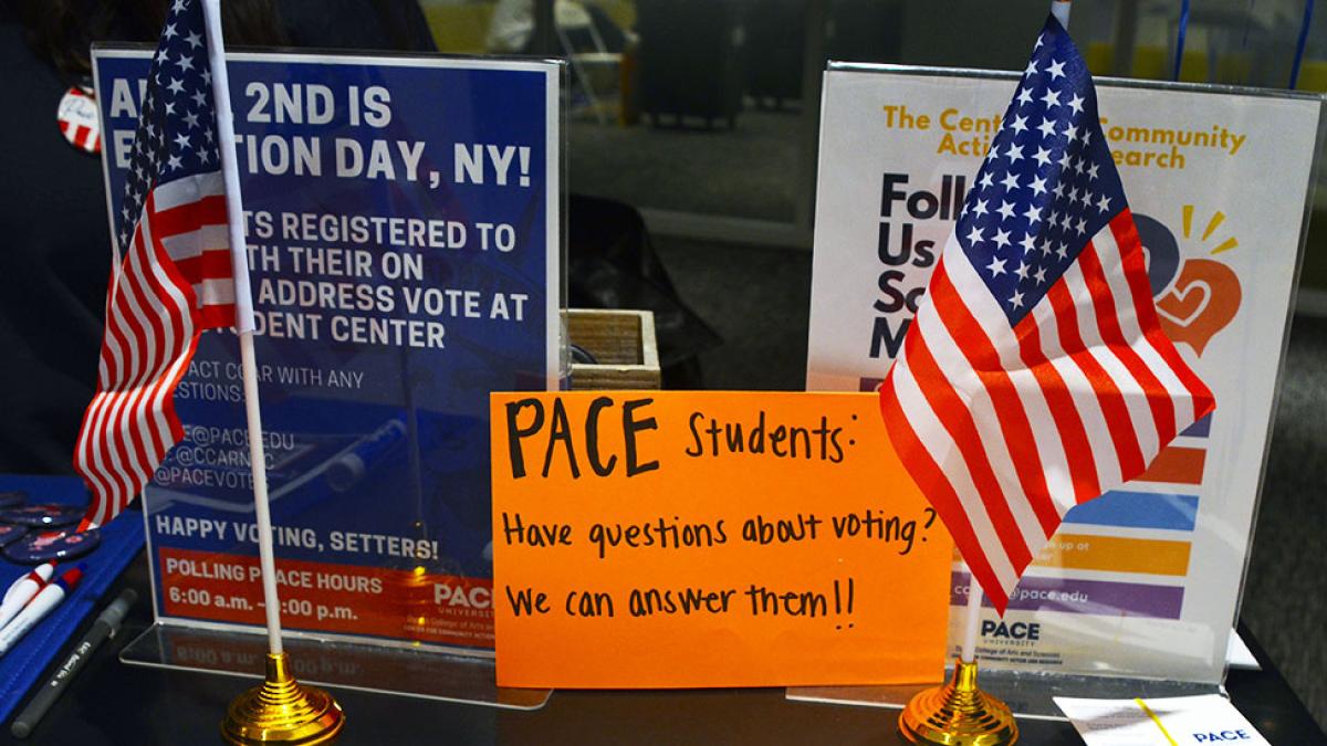 Table with flags, pamphlets, and a sign encouraging Pace University students to reach out for information about voting.