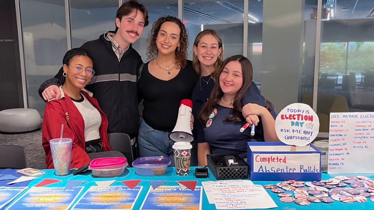 Several Pace University students smiling together behind a table with information about voting.