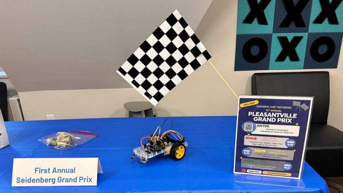 Informational table for the Pleasantville Grand Prix at Pace University, showing a small robot car built by students and a checkered flag.