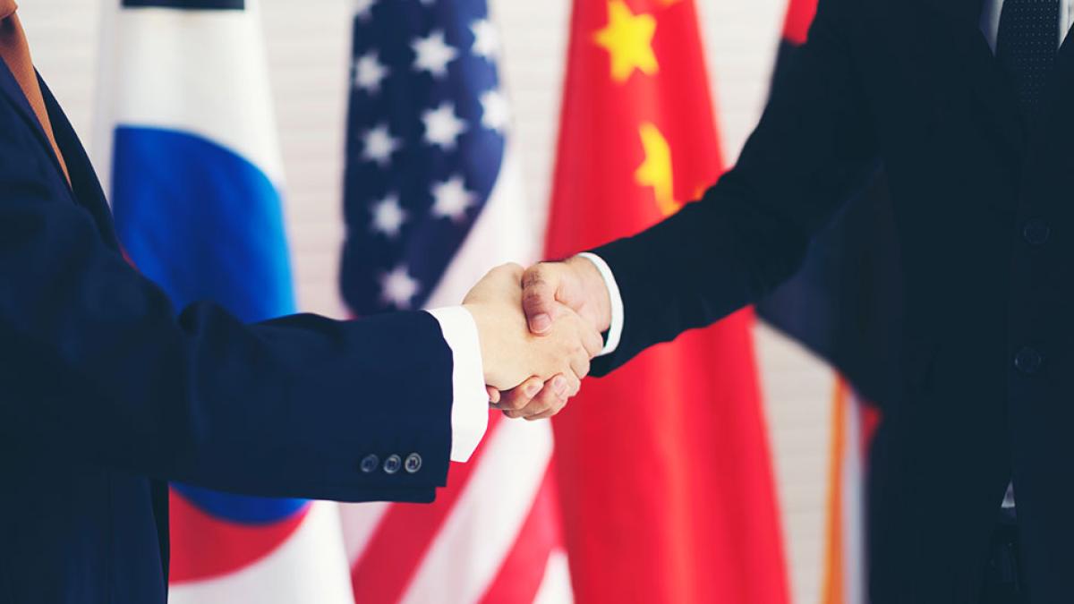 Two international diplomats shaking hands with various flags from other countries in the background