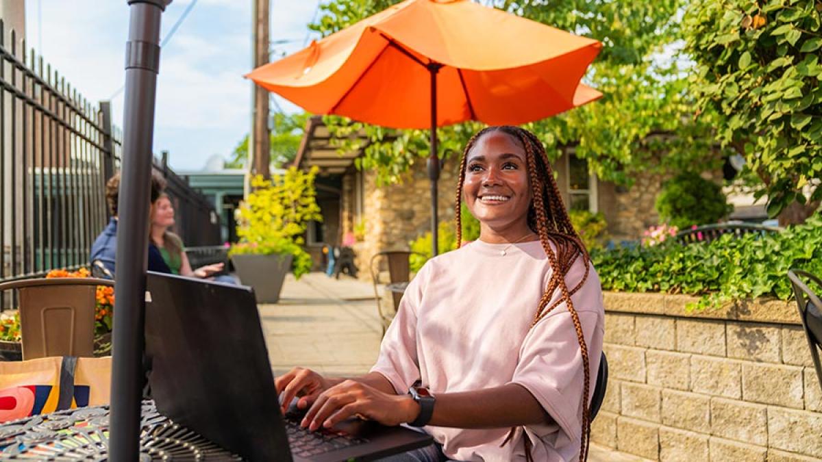 Pace University student on a laptop outside on a sunny day 