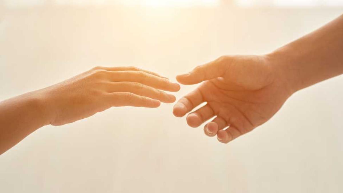 Two hands reach for eachother illuminated by a sunbeam in the background