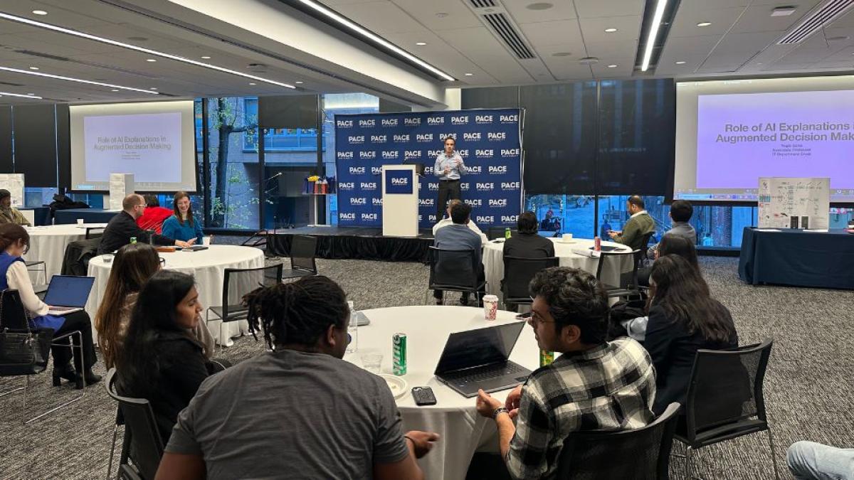 Dr. Yegin Genc, professor at Pace University's Seidenberg School of CSIS, presenting to a room full of students and faculty on a stage during the Seidenberg Annual Research Day.