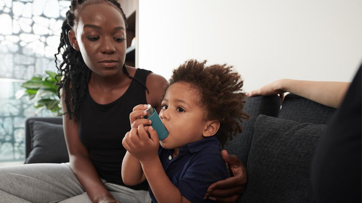 A woman watching a toddler use an asthma inhaler.