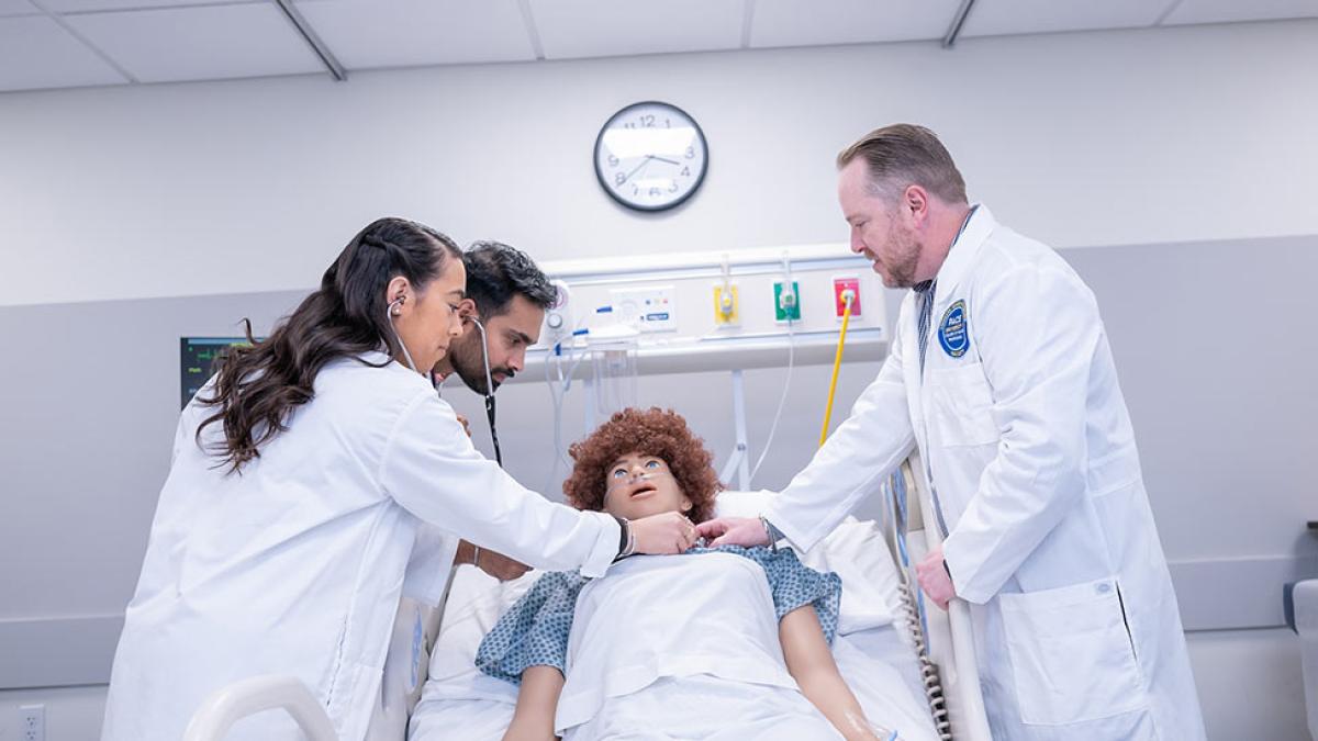 college of health professions graduate nurse practitioners practicing skills with manikin in simulation lab.