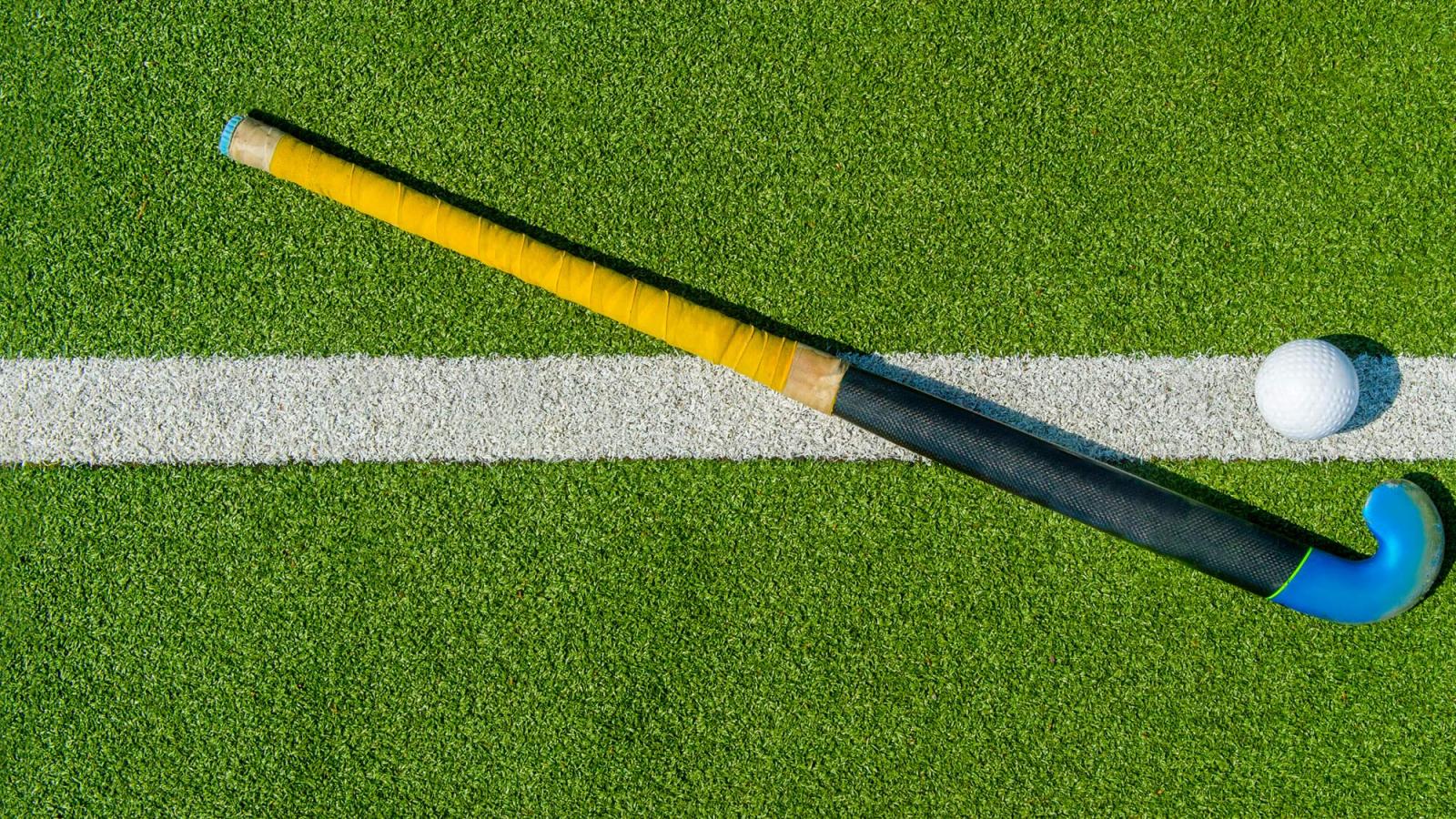 Field hockey stick and ball laying on a turf field