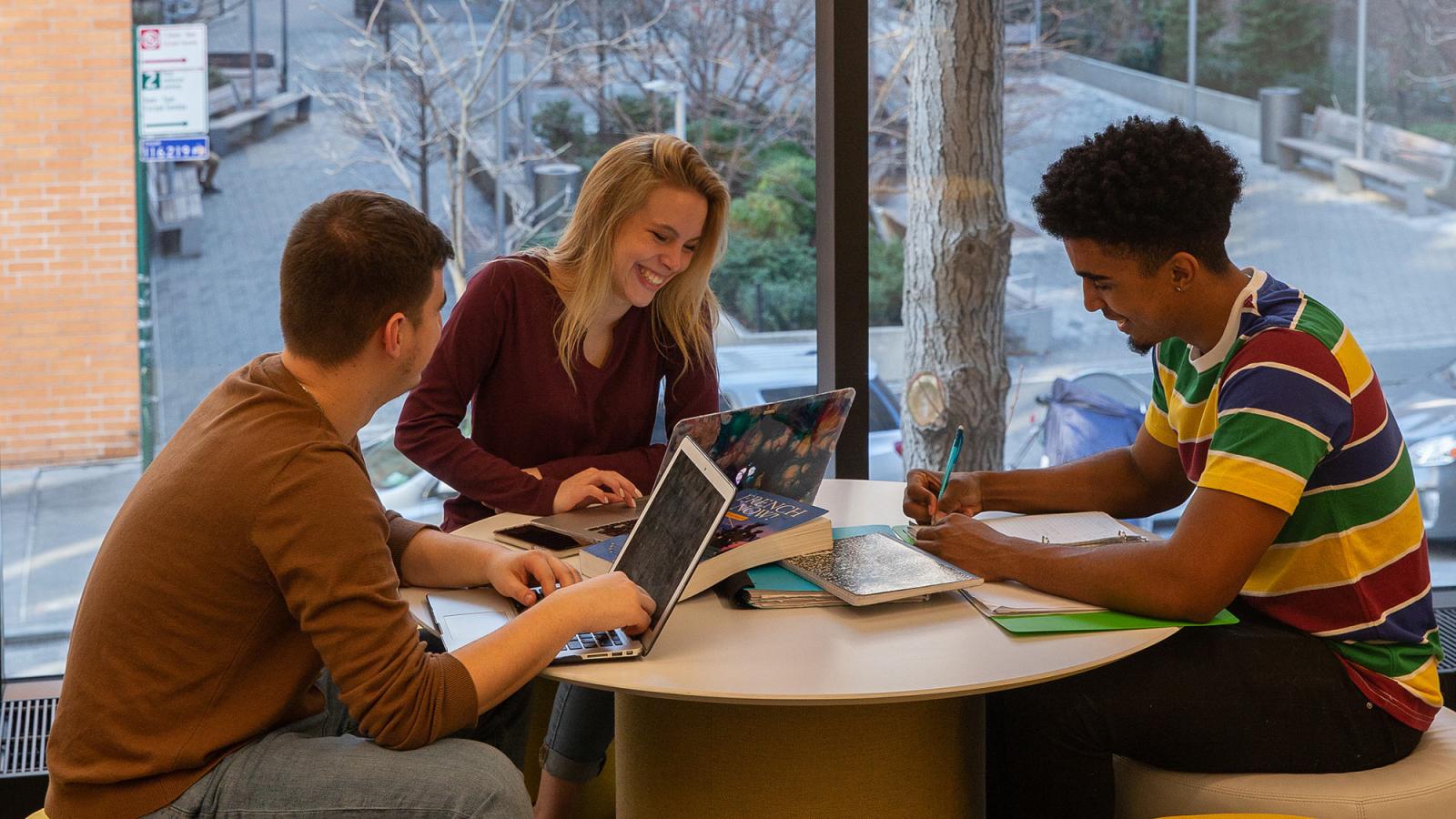 Group of students sitting at a table working on their computers.