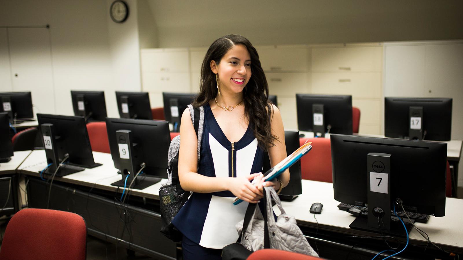 Seidenberg student standing in the middle of a classroom surrounded by computers.