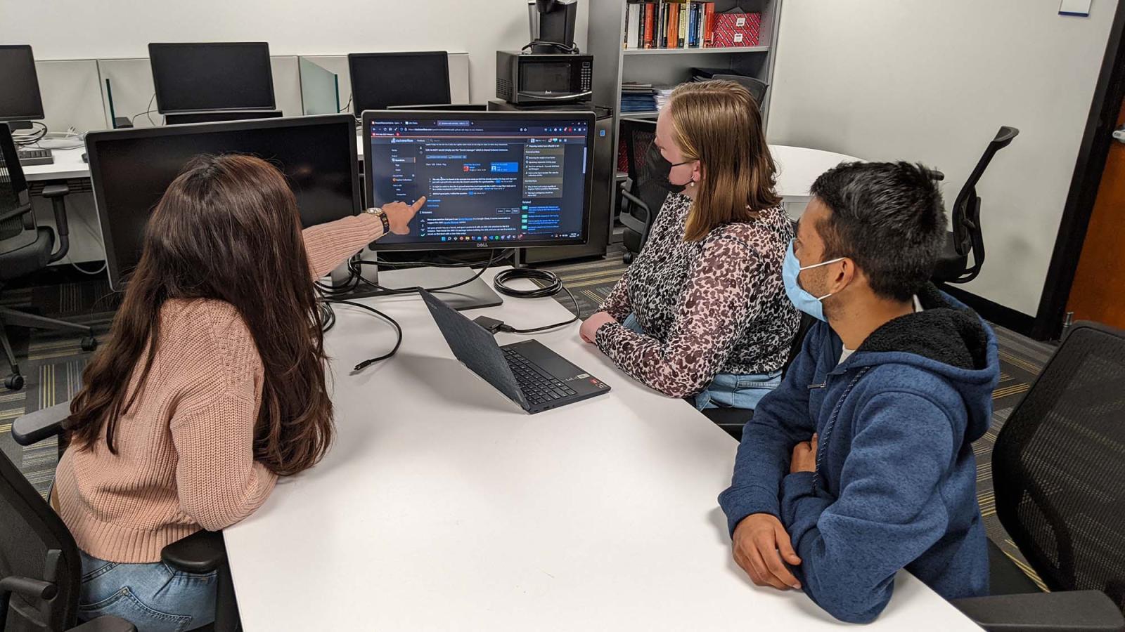 three students gather around a computer screen 