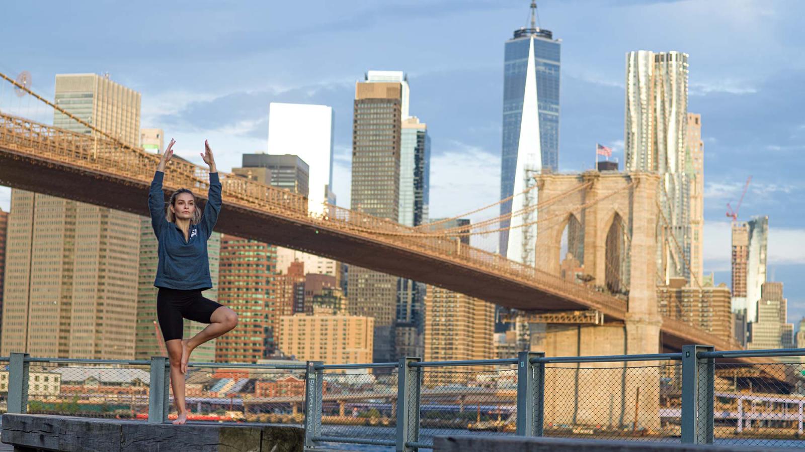 a woman performs a standing yoga pose in front of the New York skyline