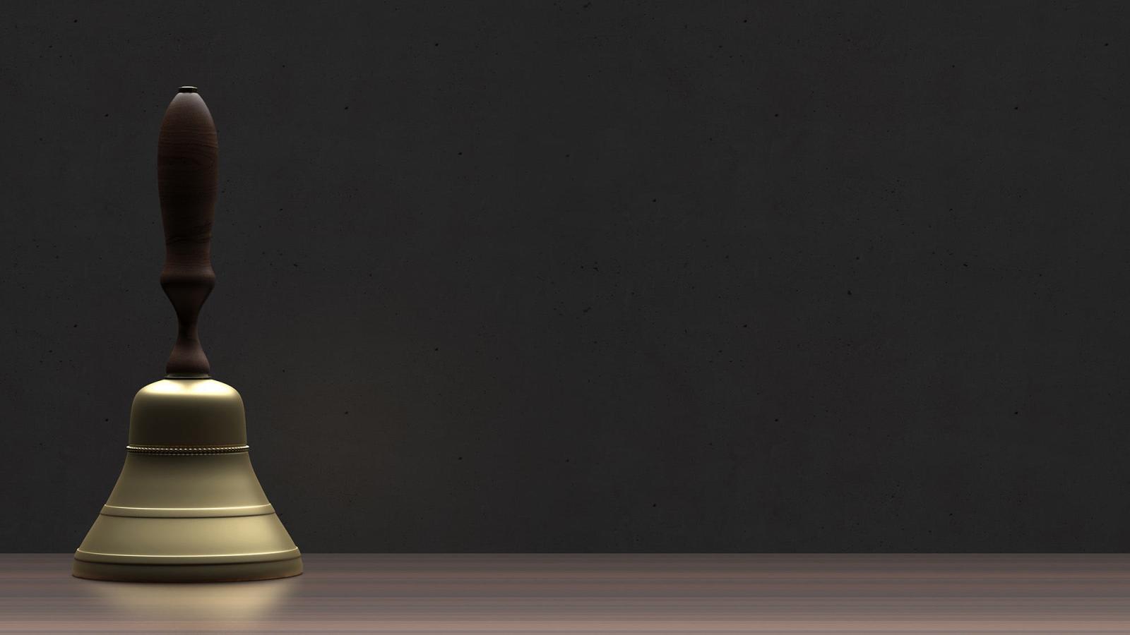 A brass bell with a wooden handle stands on a surface, in front of a dark background