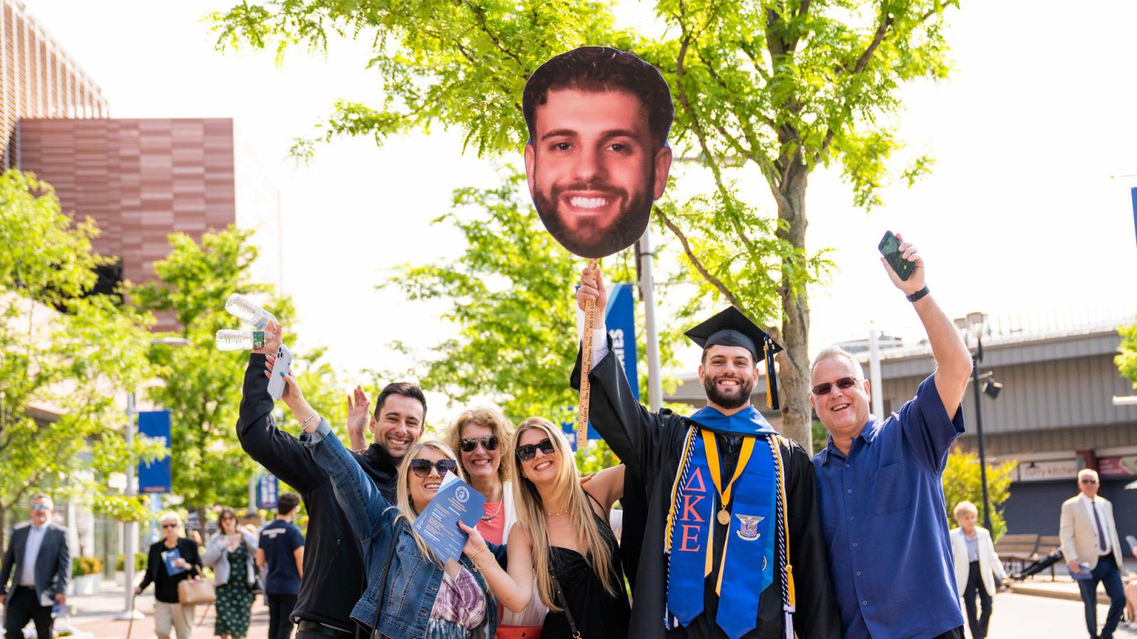 pace graduate and family holding a poster with the graduate's face on it. 