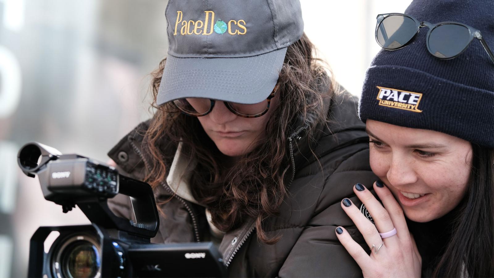 two pace students looking into the view finder of a camcorder.