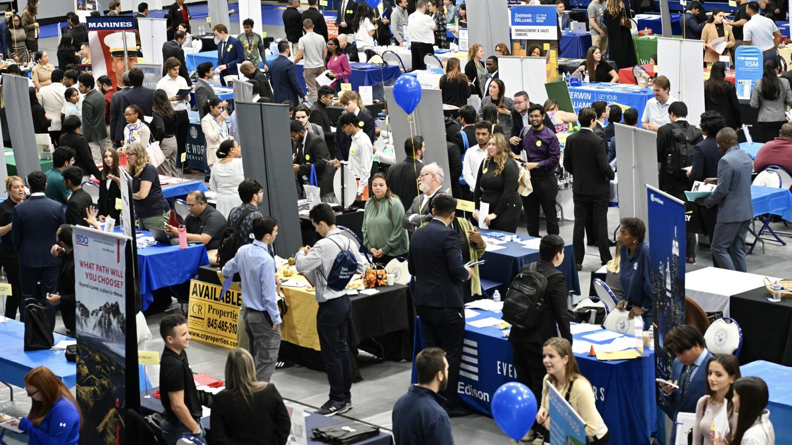 overhead view of the pace university gym during a career fair with a lot of people and display tables. 