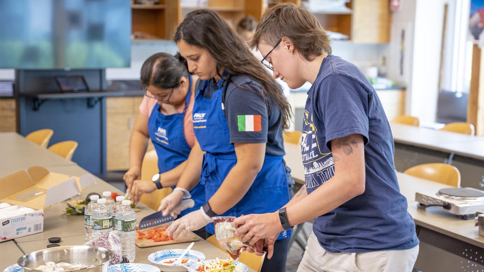 Pace students wearing aprons and working at a counter top in the teaching kitchen. 