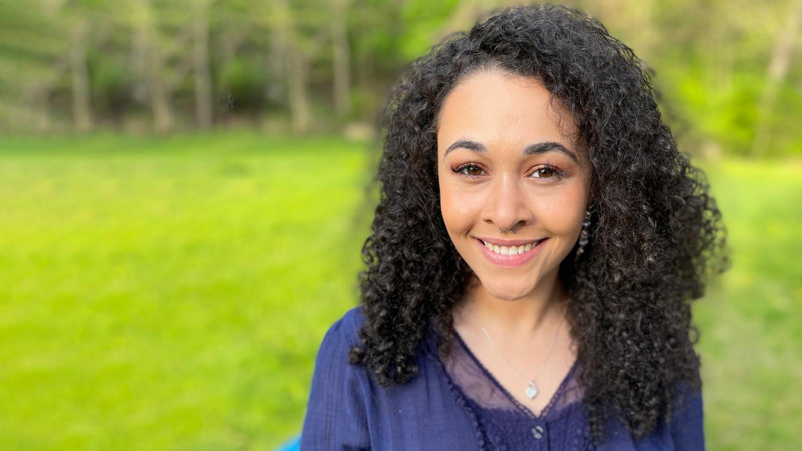 Pace student Olivia Burnett ’24 smiles and stands in front of a green lawn