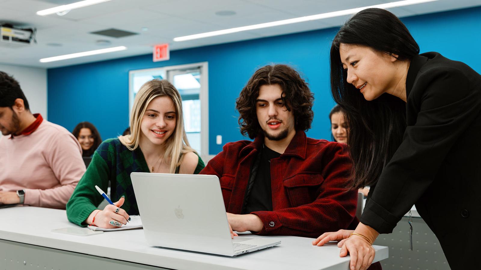 Two Pace University students studying at a computer being helped by their professor