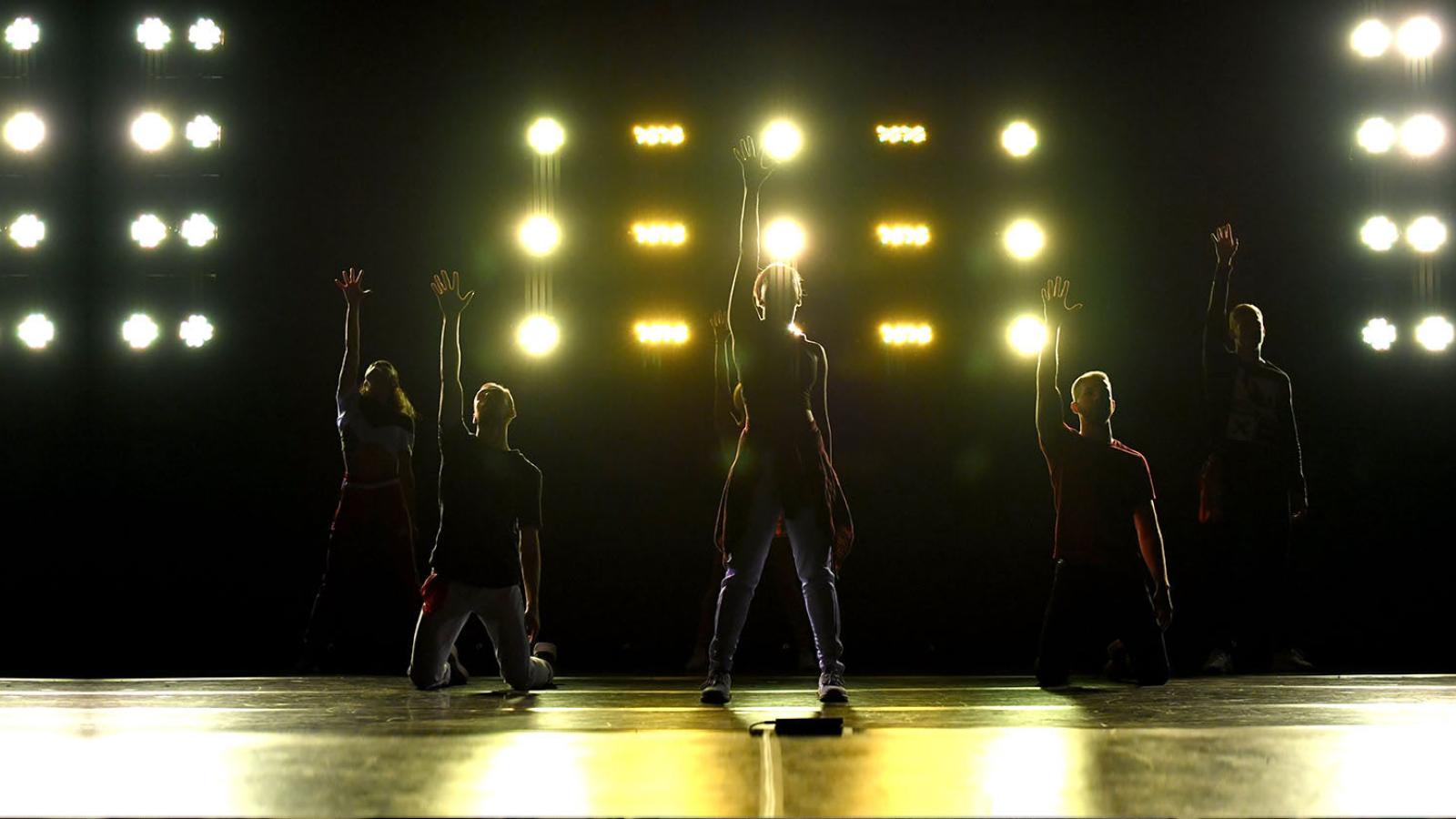 Silhouettes of Pace University students on stage in front of yellow lighting