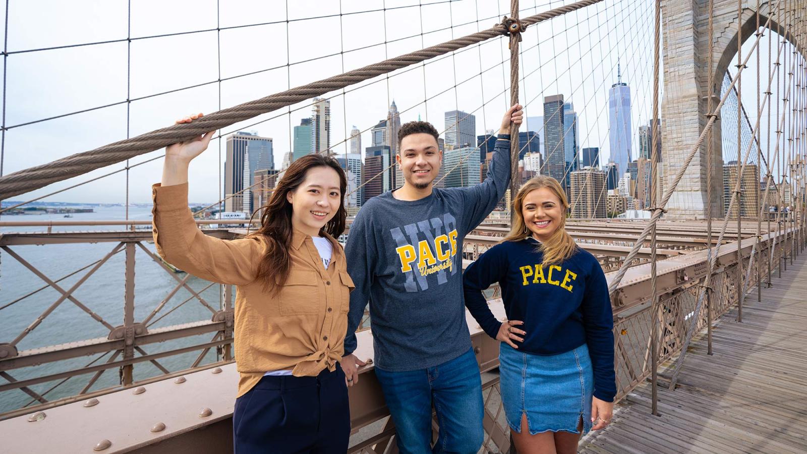 Pace University students standing on the Brooklyn bridge with the NYC skyline in the background.