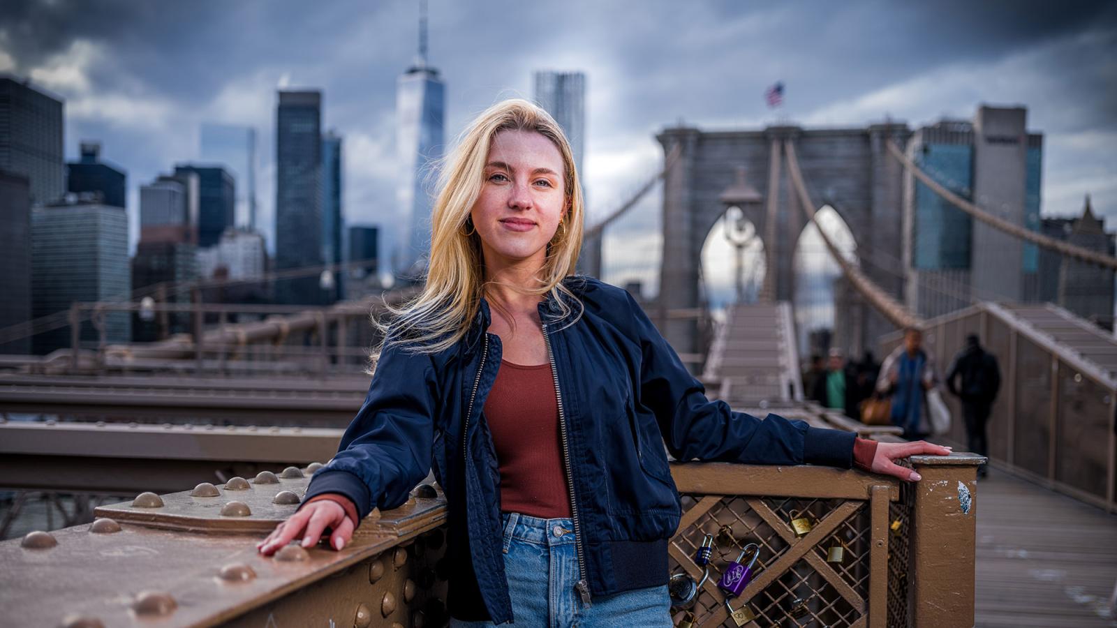 Pace University student standing on the Brooklyn Bridge with the NYC skyline in the background.