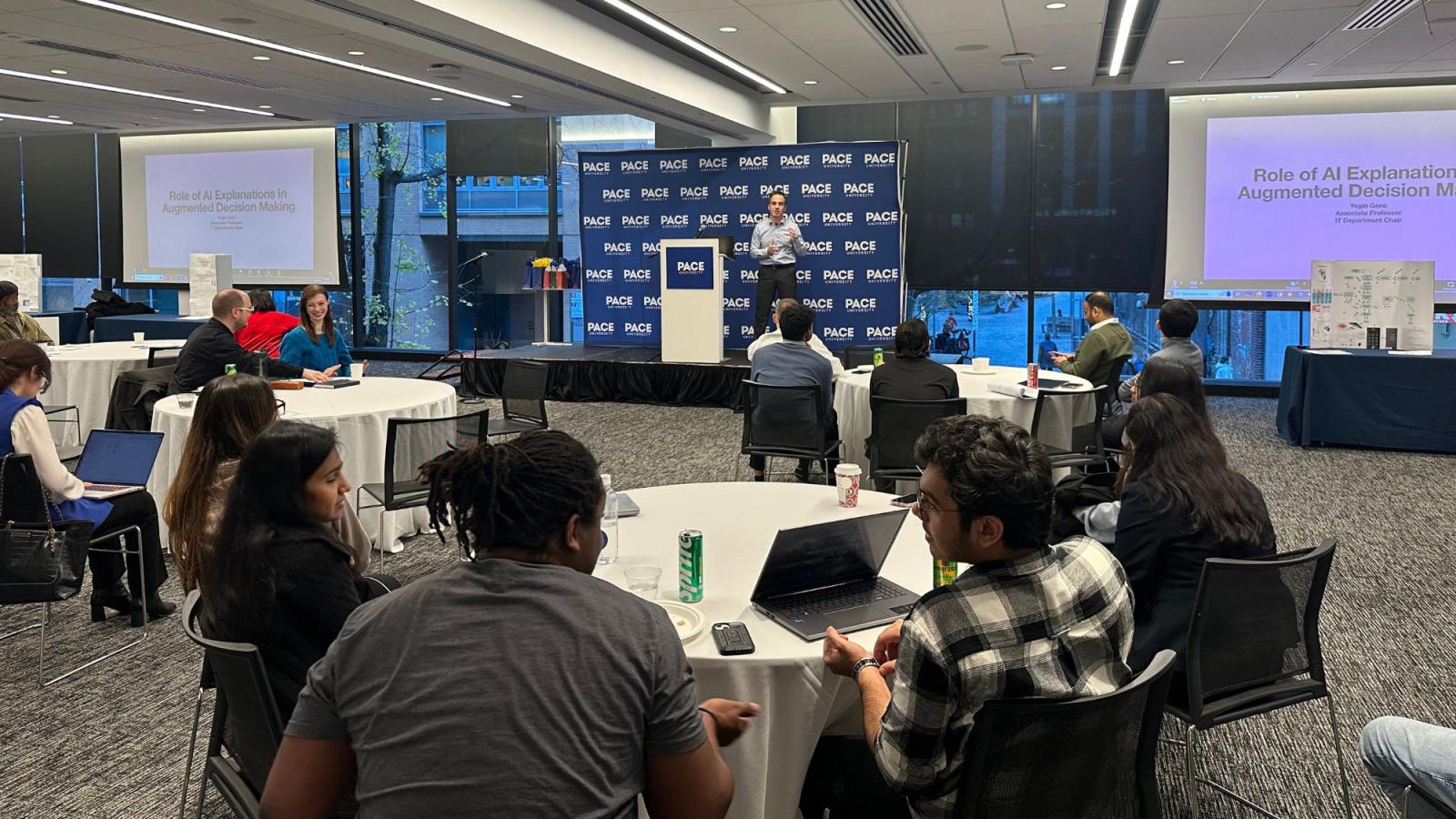 Dr. Yegin Genc presenting to a room full of students and faculty on a stage during the Seidenberg Annual Research Day.