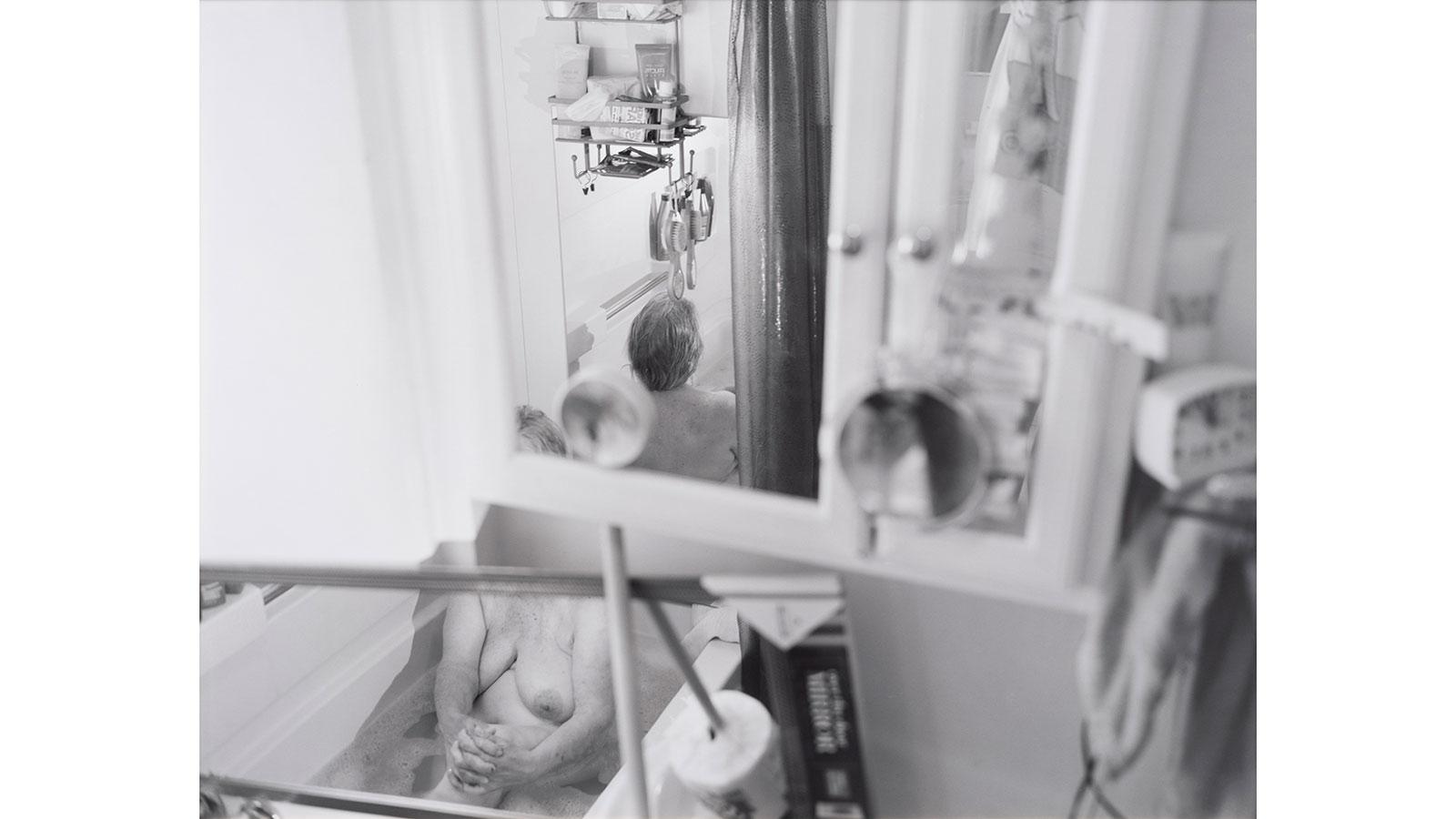 Image of an elderly lady in a bathtub called "one fifty one (syzygy)" by Katherine Hubbard displayed in the We're Home exhibition in the Pace University Art Gallery.
