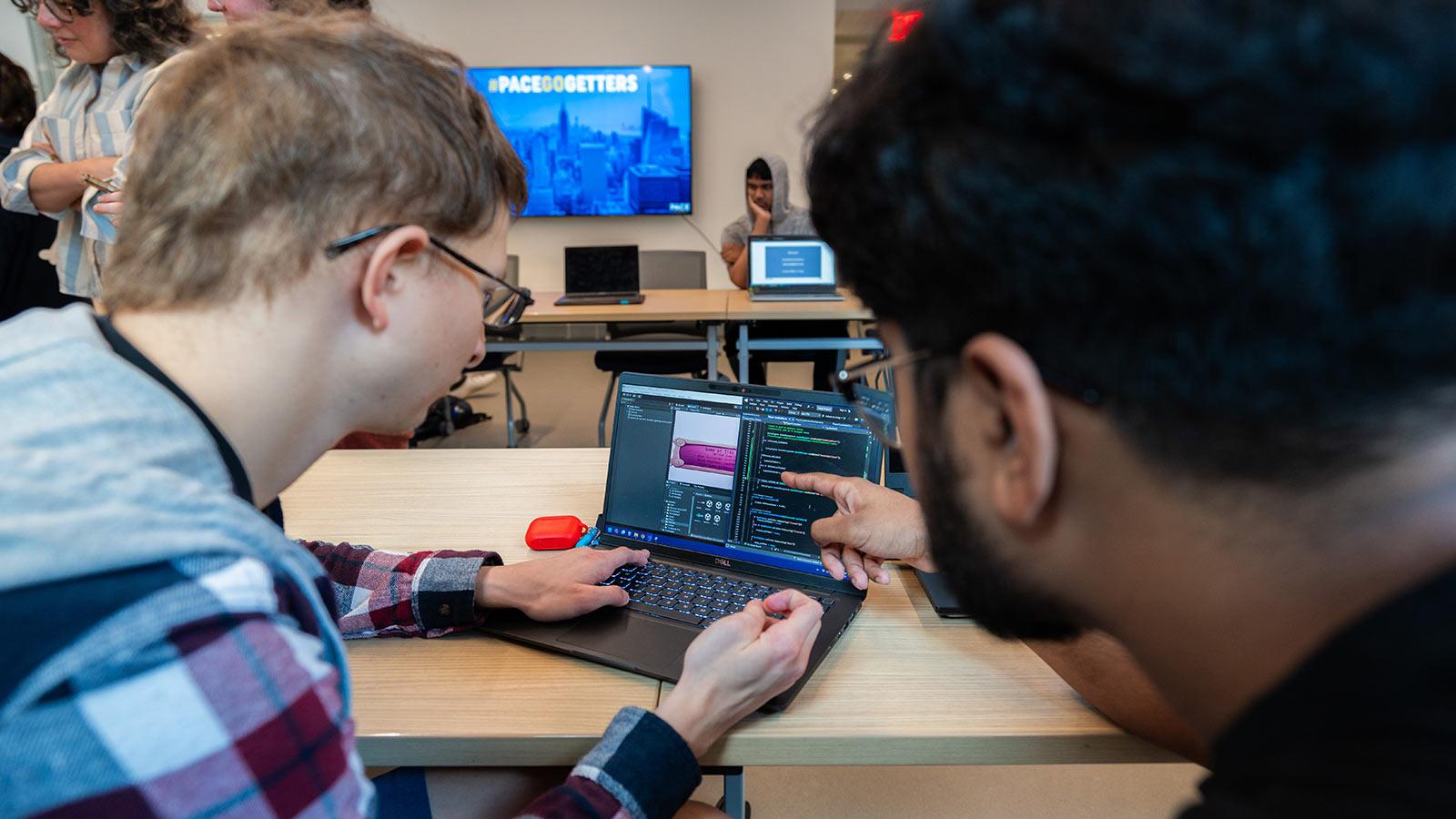 Two Pace students point at a video game on a laptop screen