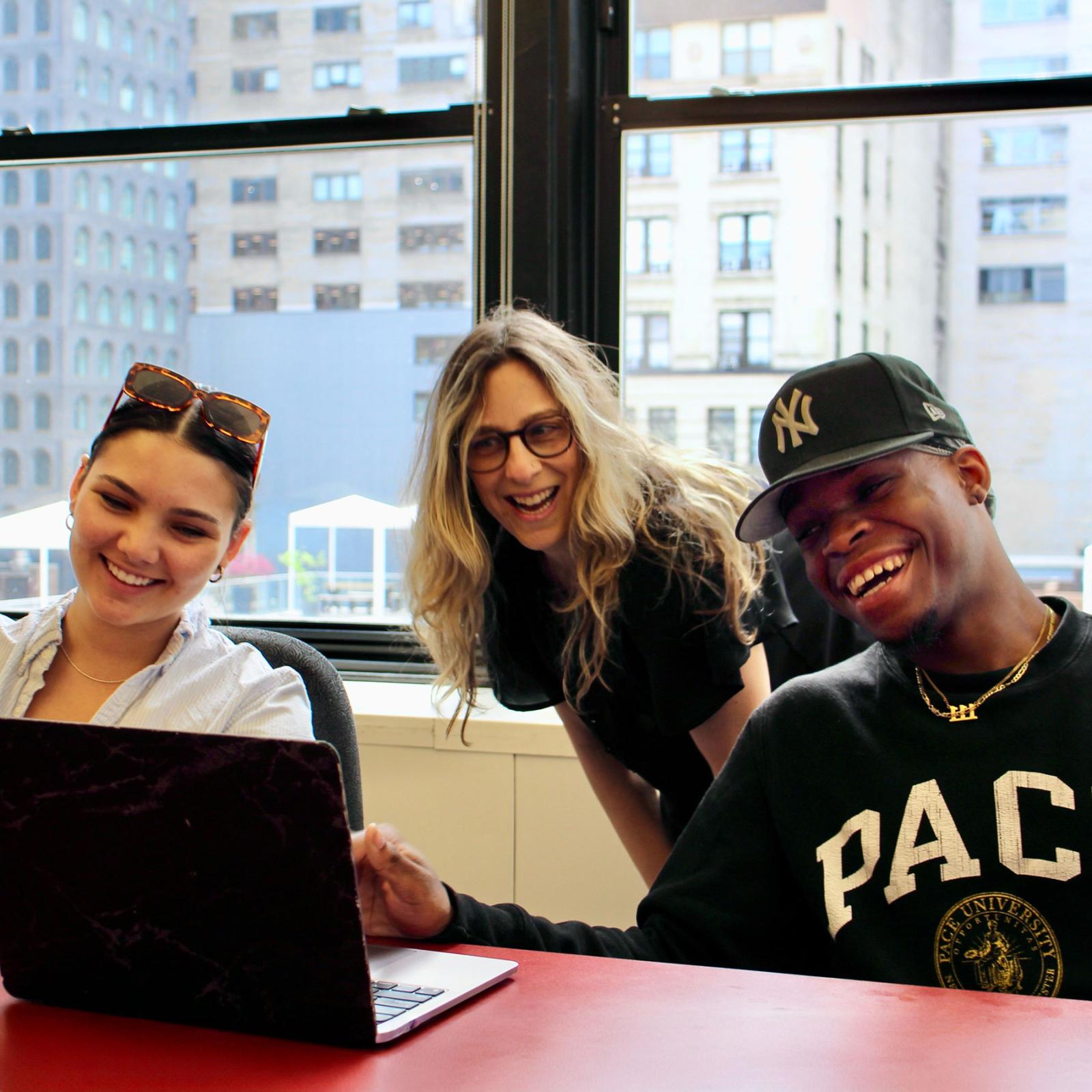 Pace University's Communication and Media Studies professor Emilie Zaslow, PhD, looking at a laptop and laughing with two of her students.