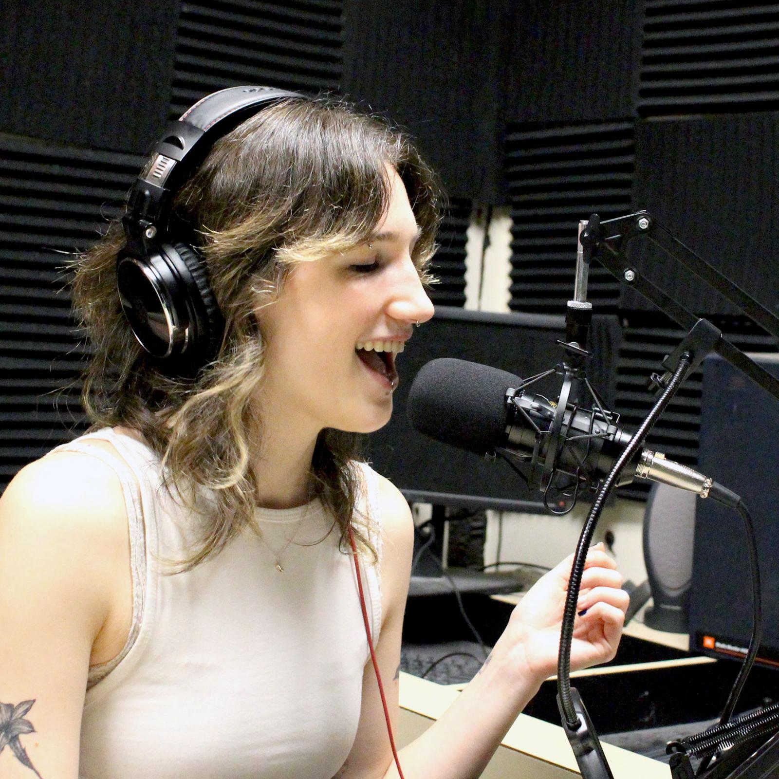 Pace University Communications and Media Studies student with a headset on and microphone talking at a radio station