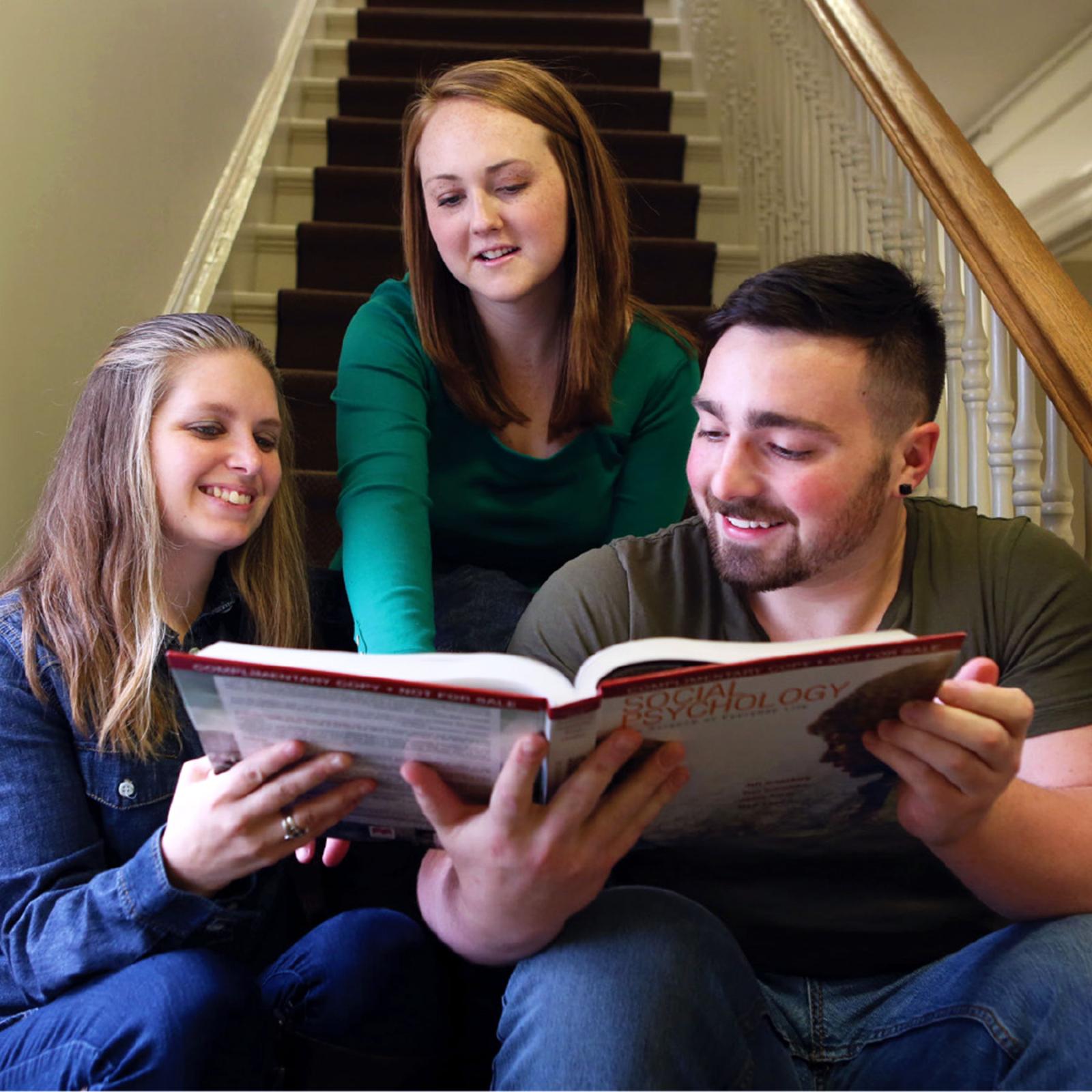 Three Pace University Psychology students look at a textbook together on a set of stairs